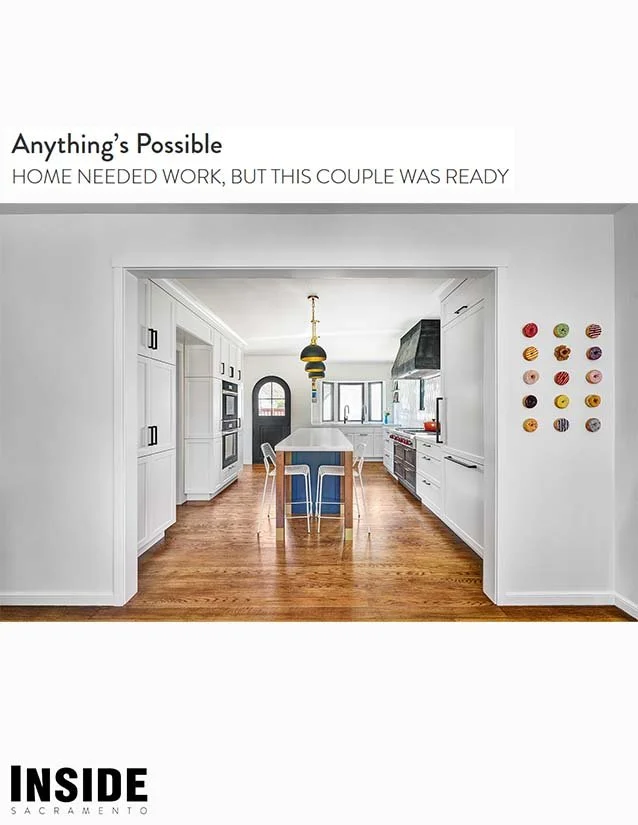Bright white kitchen with wooden floors, island with blue chairs, black pendant lights, and colorful wall decorations featuring cupcakes. Text overlay reads 'Anything's Possible. HOME NEEDED WORK, BUT THIS COUPLE WAS READY.'
