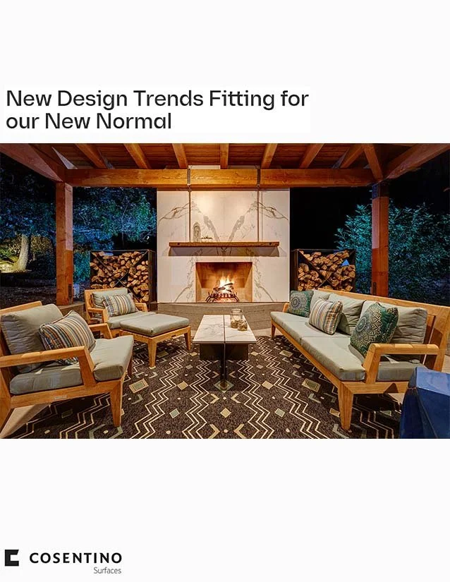 Outdoor patio with wooden beams, a central fireplace, surrounded by cushioned armchairs and a sofa with striped and patterned pillows, wood storage logs on either side, and a patterned outdoor rug.