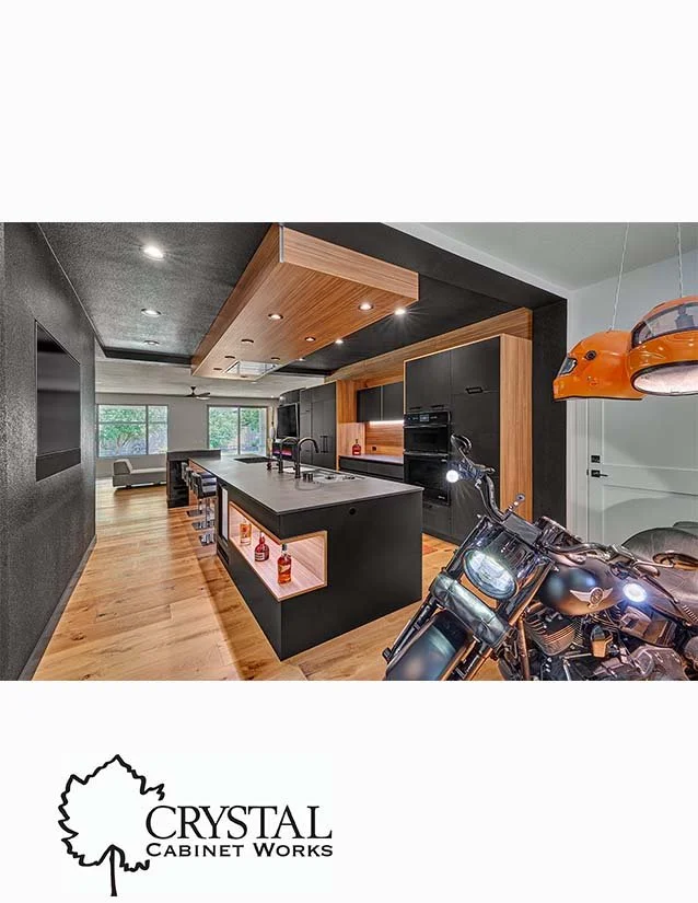 Modern kitchen with black and wood cabinets, island with built-in shelves, and a motorcycle parked nearby.
