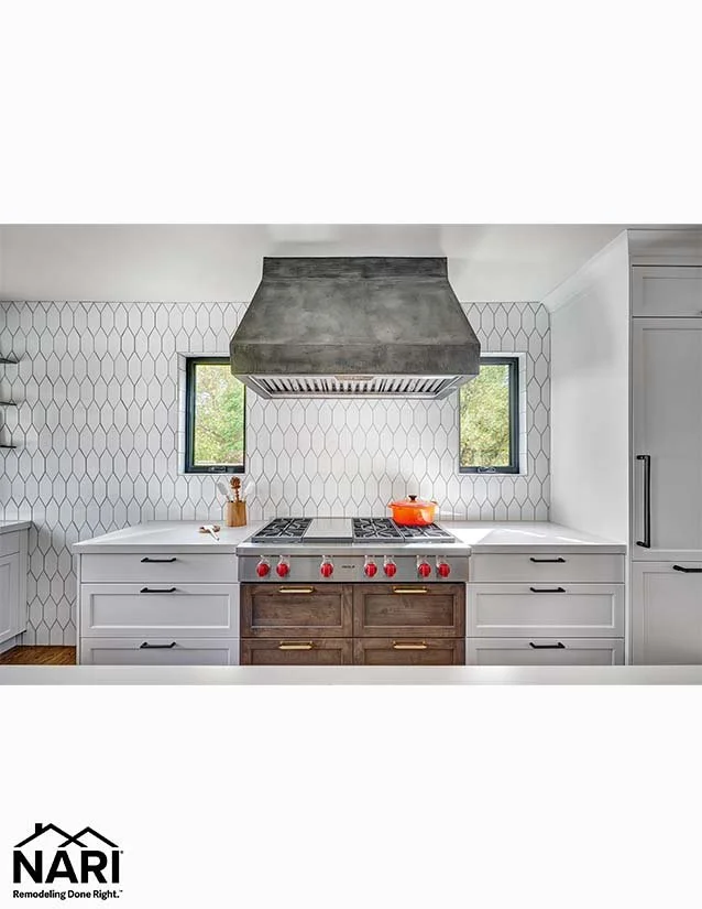 Modern kitchen with white cabinets, a gray range hood, and a stainless steel stove with red knobs, flanked by two windows.