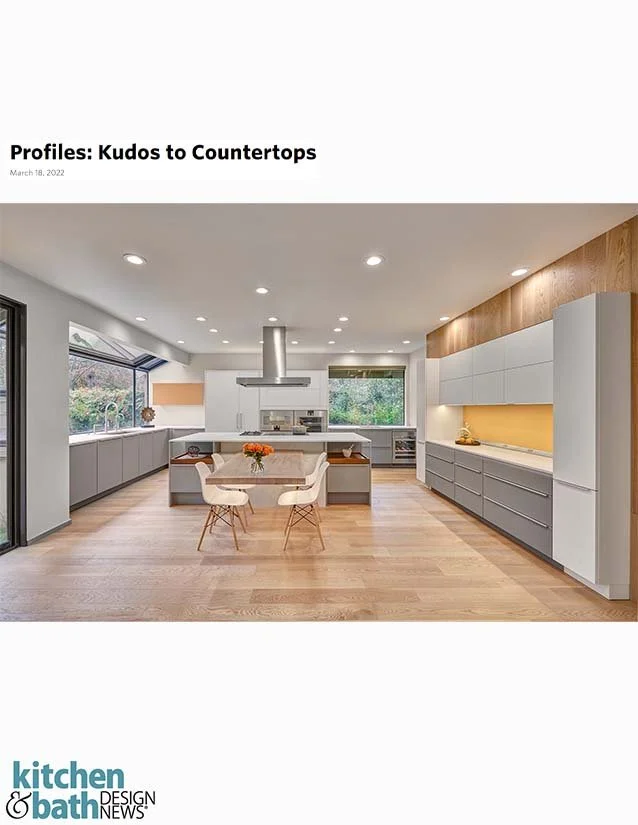 Modern kitchen with white cabinets, wooden accents, and a central island with seating, natural light from large windows, and wooden flooring.