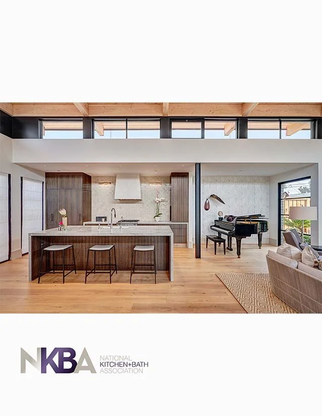 Open-concept kitchen and living area with modern decor, including a kitchen island with three stools, a grand piano, and a sectional sofa.